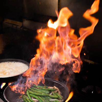 Meat and green beans frying in a flaming pan.