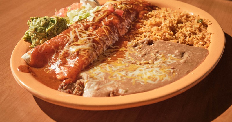 Burrito smothered in red sauce, served with salad, guacamole, sour cream, rice, and beans