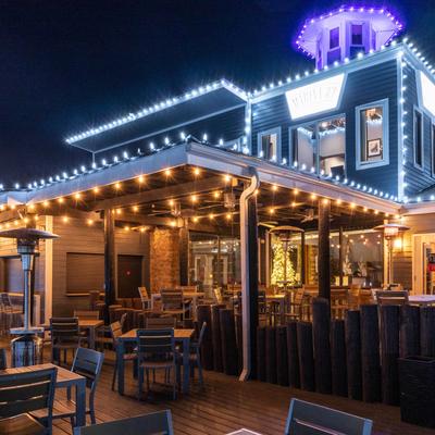 Outdoor dining area at a restaurant, decorated with string lights and patio heaters, at night.