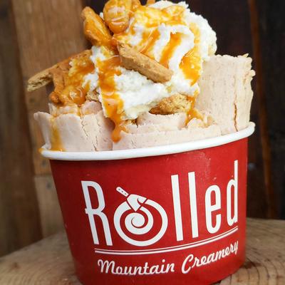 Rolled vanilla dessert with caramel drizzle in a red cup.