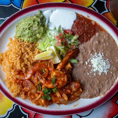 Shrimp in a red sauce served with refried beans, rice, guacamole, and salsa.