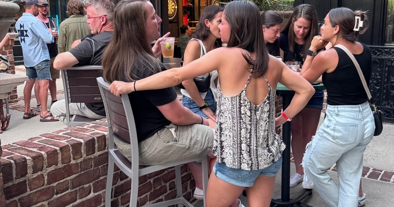 A group of people gather around an outdoor high-top table