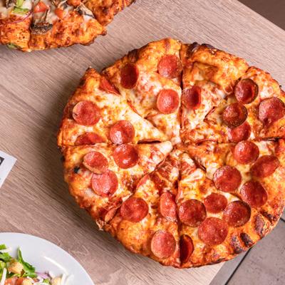 Pepperoni pizza with veggie pizza and salad on a wooden table.