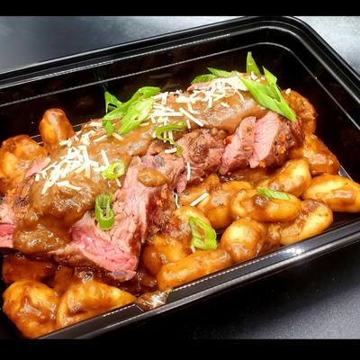 Sliced steak on gnocchi with brown gravy, topped with green onions and grated cheese.
