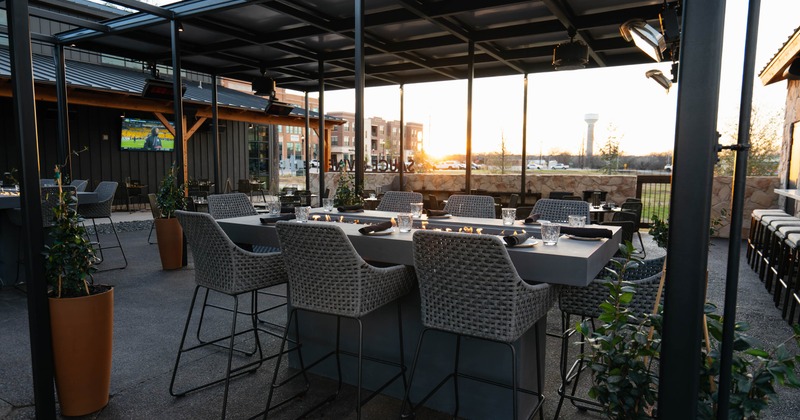 Outdoor dining area with modern furniture, fire pits, and sunset view
