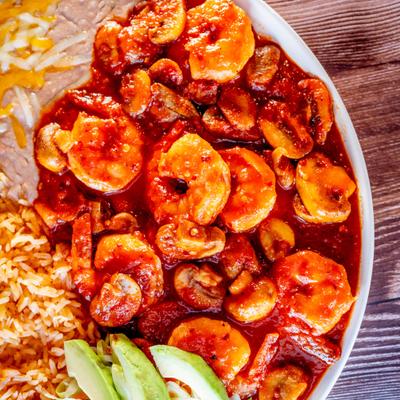 Shrimp in red sauce served with rice, beans and sliced avocado.