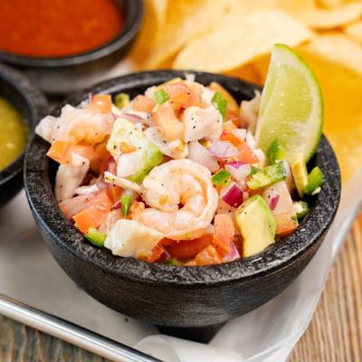 Shrimp ceviche served with diced tomatoes, onions, avocado, and a lime wedge.