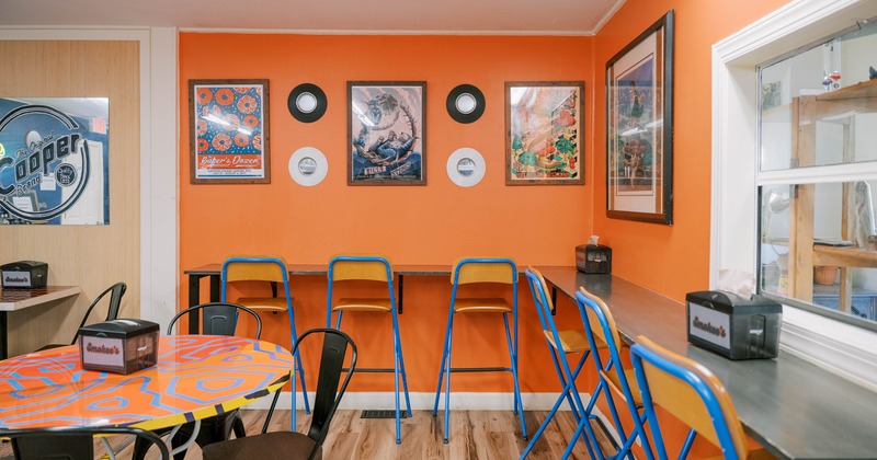A café interior with orange walls, framed posters, blue chairs, and a patterned round table