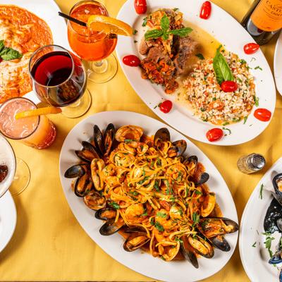 Overhead view of diverse Italian dishes, colorful cocktails and wine on a yellow tablecloth.
