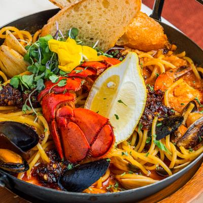 Seafood pasta with lobster tail, mussels, clams, and bread slices.