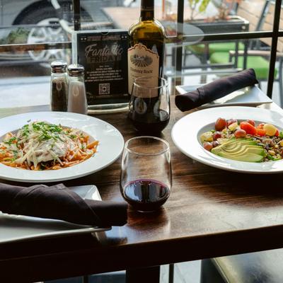 Chicken parmesan, red salad plate, and red wine served on a table by a window.