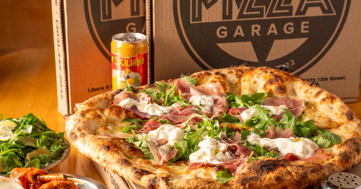 Neapolitan pizza topped with prosciutto, burrata, and arugula next to beverage cans
