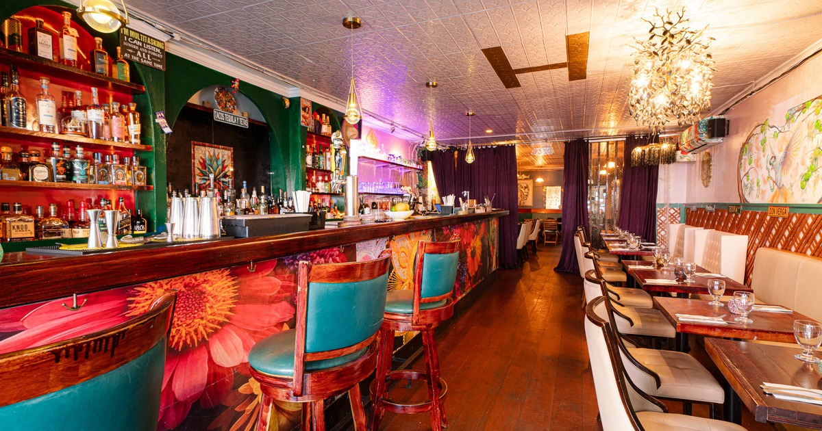 An eclectic bar and dining area with colorful decor, including a flower mural on the bar