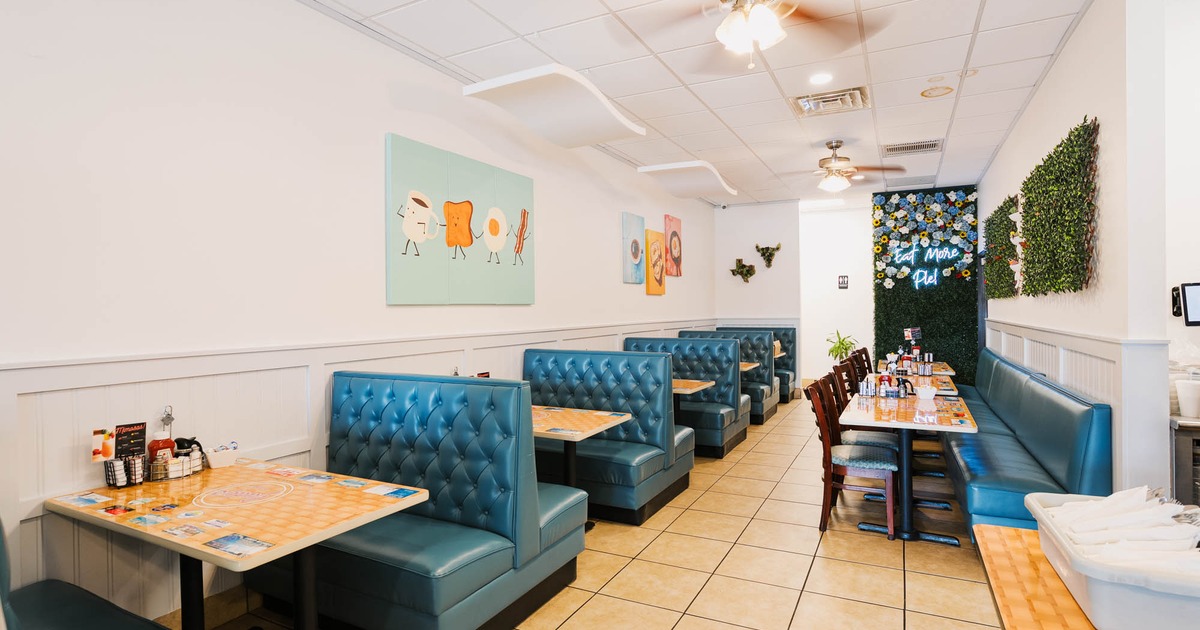 Interior of a diner-style restaurant with blue booths, wooden tables, food-themed wall art