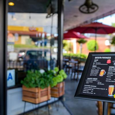 Drink menu board in front of the restaurant with seating area in the background.