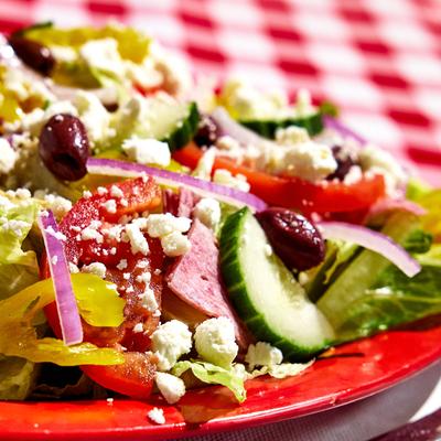 Fresh salad mix with olives and feta on a red plate.