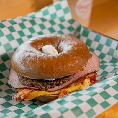 Meat Lovers bagel sandwich served on checkered paper.