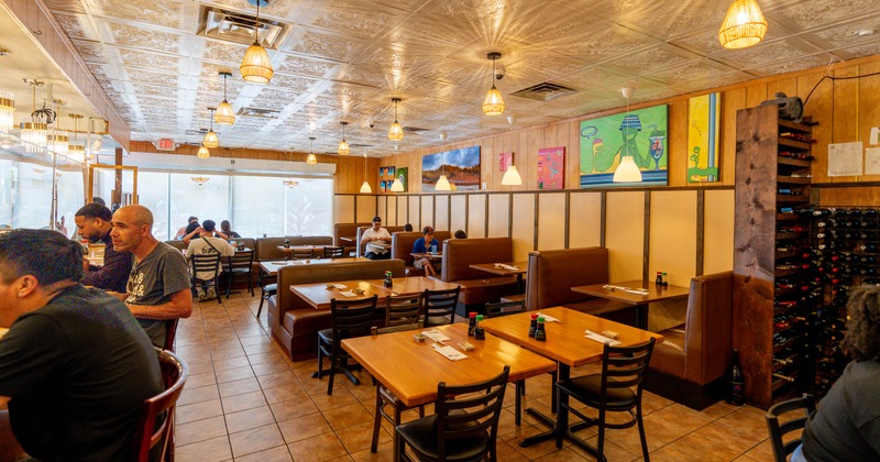 Interior of a cozy restaurant with wooden tables, brown booths, and patterned ceiling