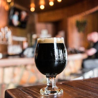 A glass of dark beer on a table with a bar in the background.