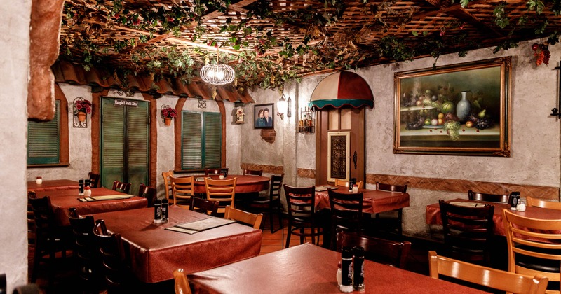 Interior with red tablecloths, wooden chairs, a decorative ceiling, and wall art.