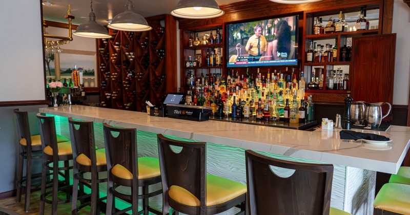 Modern bar with white countertop, high chairs, liquor shelves and mounted television