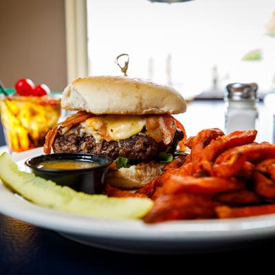 Gouda burger with a pickle spear, sauce, and  sweet potato fries on the side.