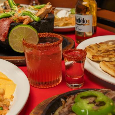 Red cocktail, tequila shot, and Mexican dishes on a red table.