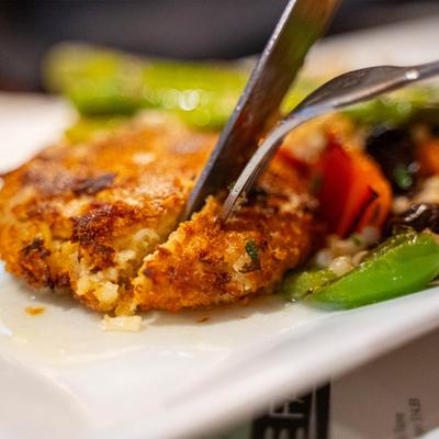 Fork and knife cutting into a crab cake and vegetables, close up.