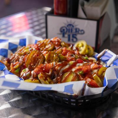 Loaded fries with pickles, jalapenos, and sauces on a table.
