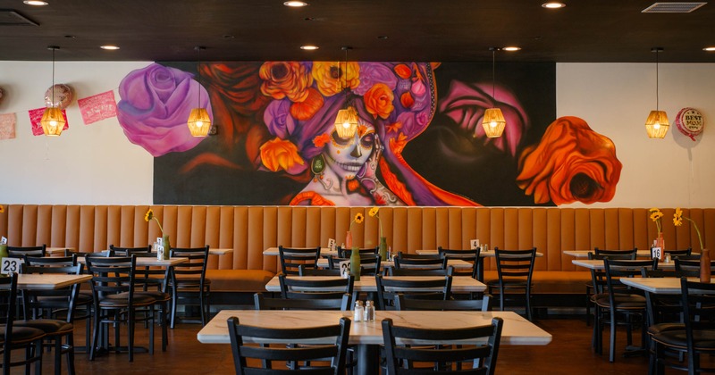 Interior, vibrant Day of the Dead mural and rows of tables and chairs, banquette seating