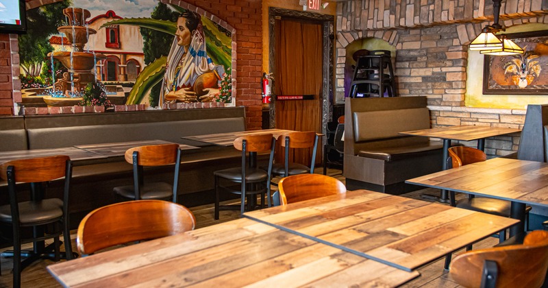Interior of a restaurant with wooden tables, chairs, a mural, and stone-patterned walls