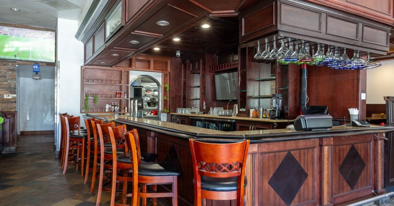 Interior view of a bar with wooden counter and stools, a TV displaying a sports game