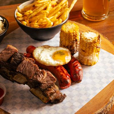 Grilled meats with corn on the cob, fried egg, and fries.