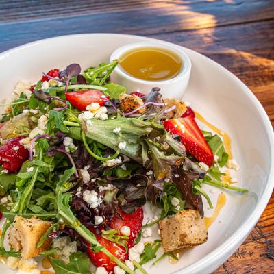 Salad featuring fresh strawberries, arugula, feta cheese, croutons and a dressing.