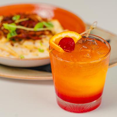 Tequila Sunrise in front of a plate of bacon mac and cheese.