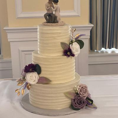 A three tier wedding cake with floral decoration and wedding couple figurines on top
