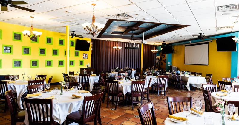 Restaurant interior with tables set with white linens, yellow napkins, and floral centerpieces