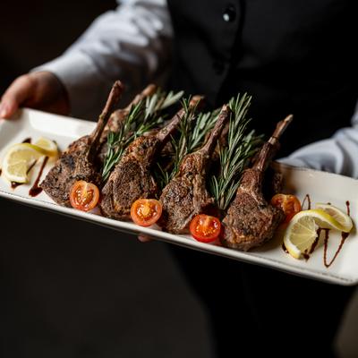 Served holding a tray of lamb chops with rosemary, tomatoes, and lemon slices.
