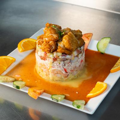 Ceviche tower topped with fried shrimp on a plate with sauce and orange garnish.