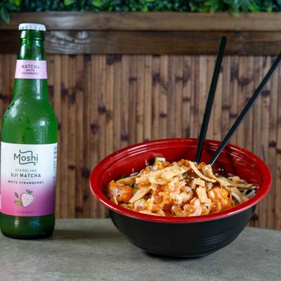 Poke bowl served with chopsticks and a bottled drink on a table.
