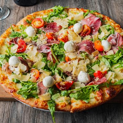 Pizza with arugula, prosciutto, cherry tomatoes, shaved Parmesan, and mozzarella cheese.