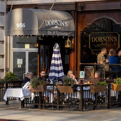 Outdoor restaurant patio with patrons dining under a large awning.