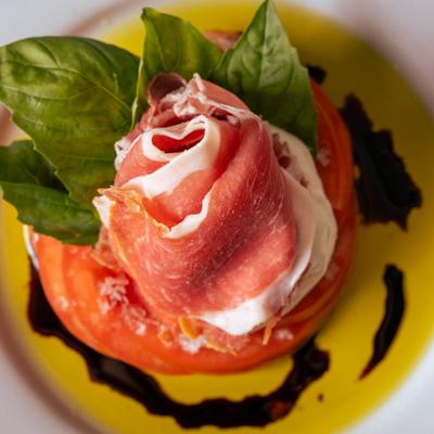 Prosciutto wrapped over burrata on tomato slices with balsamic-drizzled olive oil.