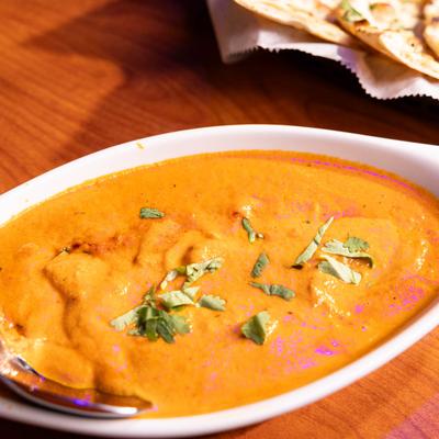 A bowl of creamy orange  curry garnished with herbs.