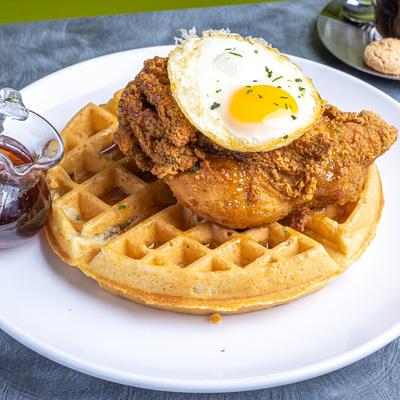 Dhicken and Waffles topped with fried egg and served with syrup on the side.