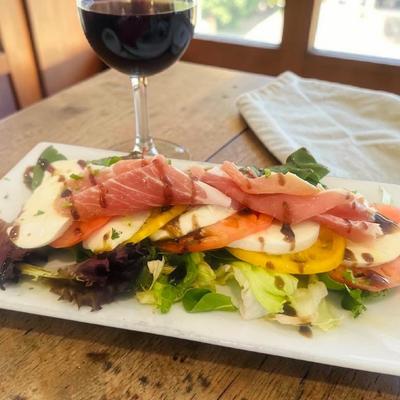 Caprese salad topped with prosciutto and served with a glass of red wine.