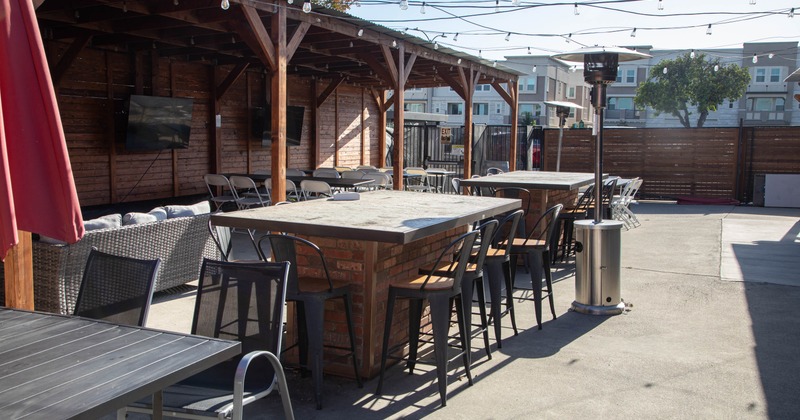 Outdoor seating area with wooden beams, brick tables, and high stools