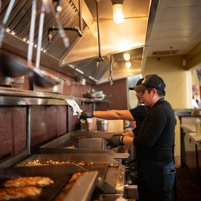 Kitchen staff cooking on a flat top grill.