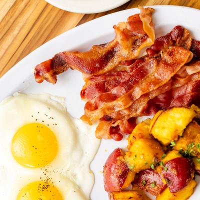 A plate of two sunny side up eggs, home potatoes, and crispy bacon.