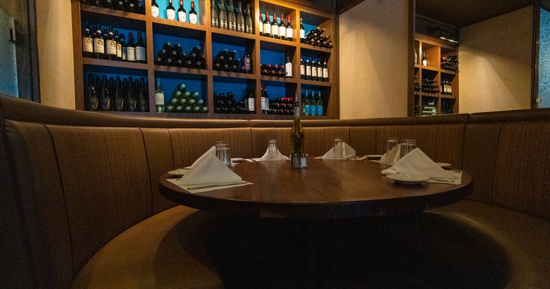 Interior, booth with a semi-circular table, napkins and glasses, shelves filled with wine bottles